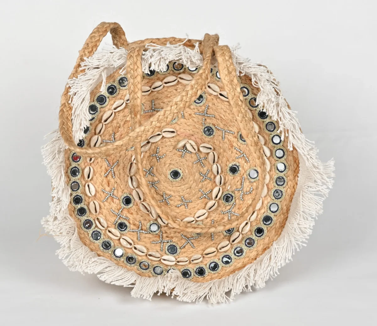 Explore the BANJARA handcrafted round jute handbag featuring mirrors, cowrie shells, and fringe. A perfect boho beach bag that blends artisanal charm with utility.