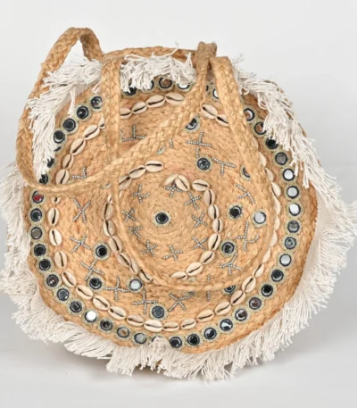Explore the BANJARA handcrafted round jute handbag featuring mirrors, cowrie shells, and fringe. A perfect boho beach bag that blends artisanal charm with utility.