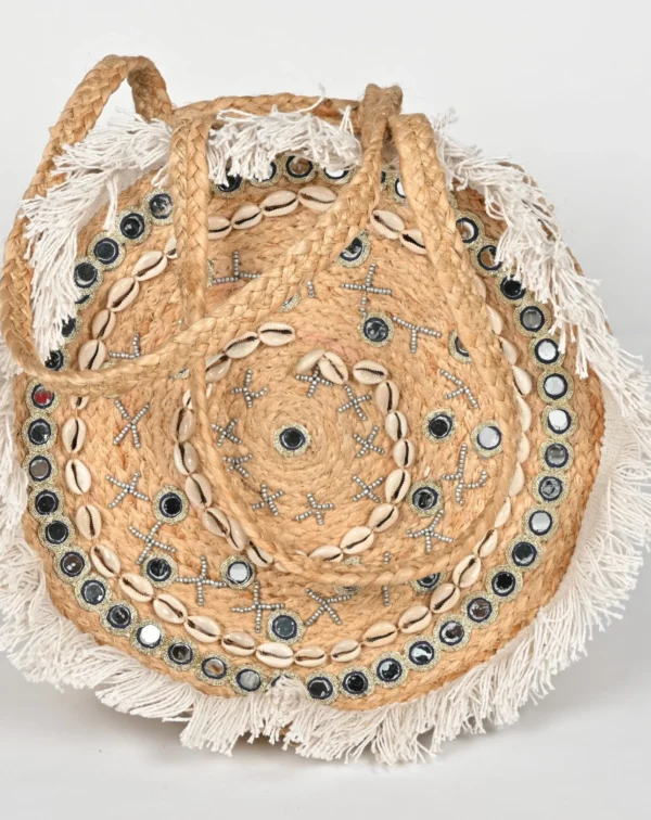 Explore the BANJARA handcrafted round jute handbag featuring mirrors, cowrie shells, and fringe. A perfect boho beach bag that blends artisanal charm with utility.