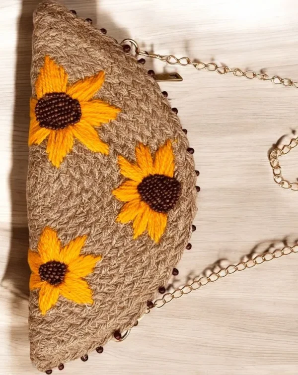 Make a sunny statement with the ATICUE half moon jute clutch. Features hand-embroidered sunflowers, zipper closure, and gold shoulder chain for effortless charm.